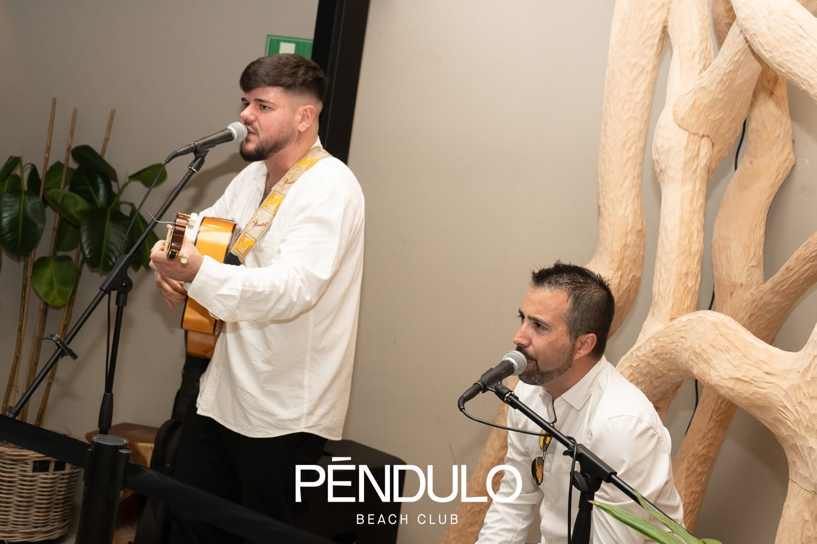 Dúo acústico cantando con guitarra y micrófonos en un evento interior