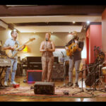 Grupo de rumba tocando en directo en una sala cálida con cantante, guitarra, bajo, teclas y percusión