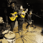 Grupo de rumba en directo con guitarras, percusión y micrófonos en escenario