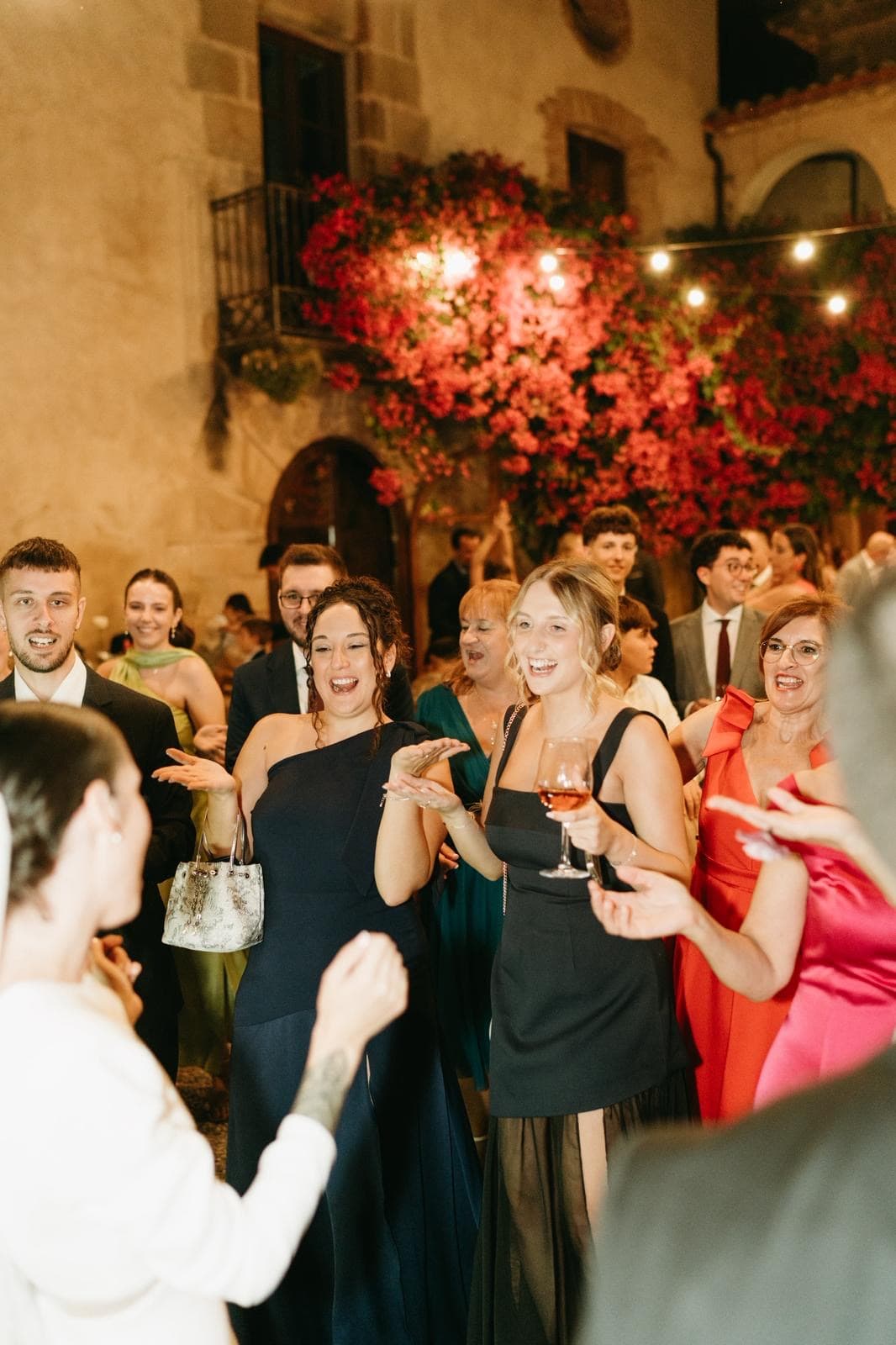 Invitados de boda aplauden y cantan bajo luces en un patio nocturno