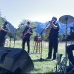 Banda tocando en un prado con invitados y montañas, ambiente de fiesta y baile
