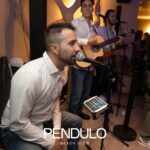 Trío musical en directo: cantante sentado y dos guitarristas ante público