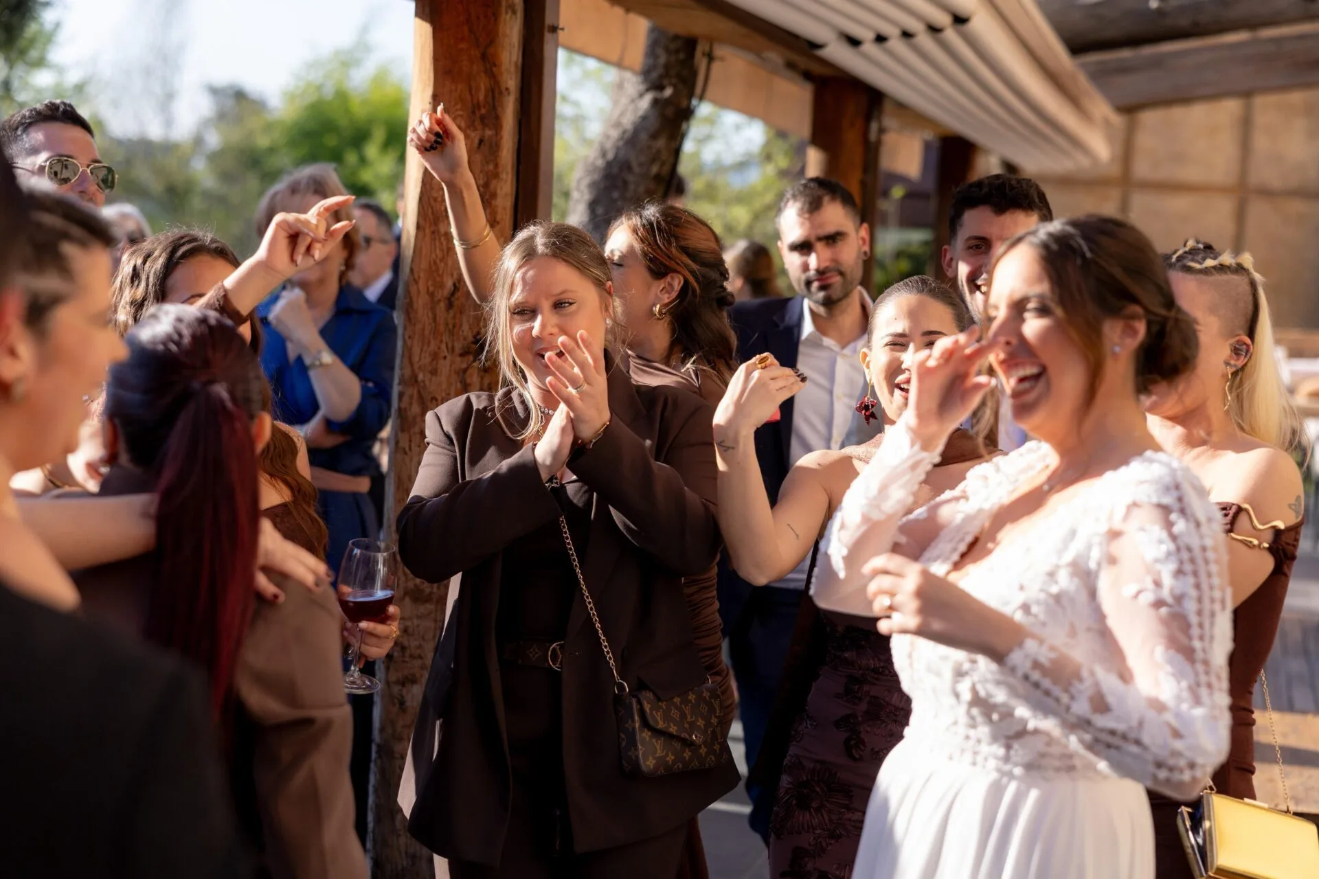 Grupo de invitados bailando y aplaudiendo en una celebración al aire libre; en primer plano una mujer con vestido blanco sonríe mientras otras personas levantan los brazos y siguen el ritmo, un ambiente festivo ideal para rumba catalana con toque urbano para la noche en Barcelona.