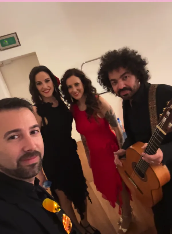 Selfie en un camerino con cuatro integrantes de un grupo: dos mujeres vestidas de negro y rojo sonriendo, y dos hombres; uno sostiene una guitarra española. Imagen previa a una actuación, ideal para rumba fusión y pop flamenco para eventos de empresa en Barcelona.