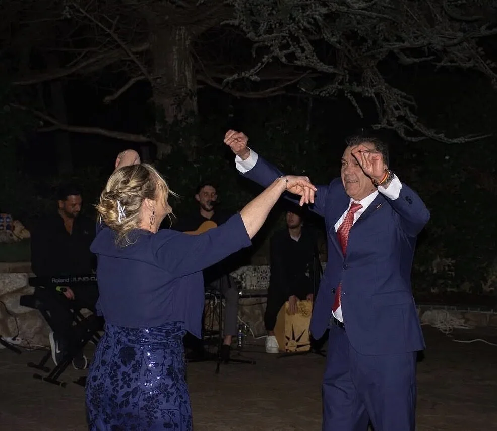 Una pareja de invitados baila con los brazos en alto en una celebración nocturna al aire libre; al fondo se ven músicos con guitarra, teclado y cajón, creando un ambiente de dúo de flamenquito y rumba catalana para bodas en Barcelona.