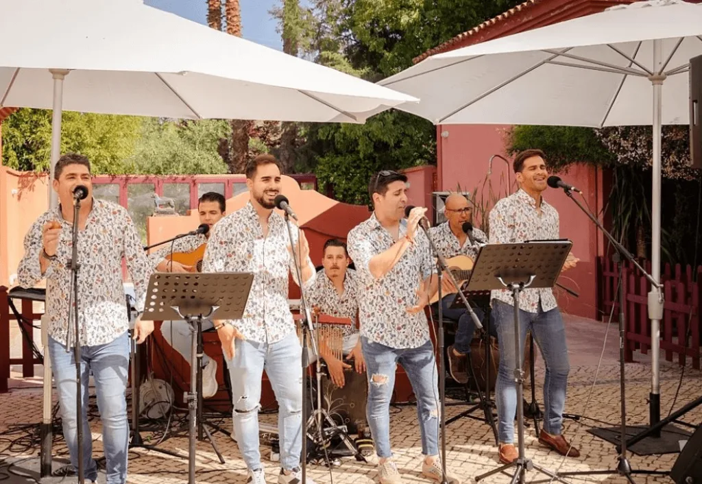 Grupo de rumba y flamenquito con varios cantantes y guitarristas actuando en un patio al aire libre, bajo grandes sombrillas blancas y con micrófonos y atriles; una imagen ideal para rumba y flamenquito para bodas con buen rollo en Badajoz.