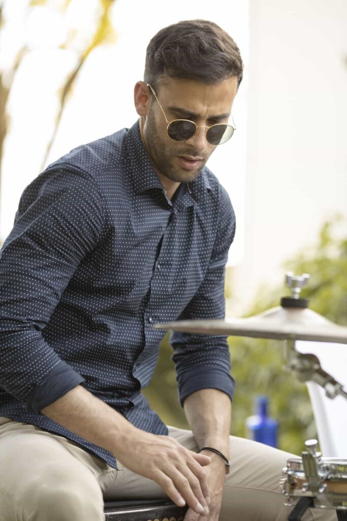 Primo piano di un percussionista seduto, con occhiali da sole e camicia blu a pois, che guarda verso il basso mentre suona; a destra si vede un piatto della batteria. Immagine adatta a raccontare flamenquito e rumba fusione per matrimoni a Cordova in formato trio.