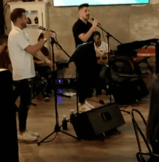 En un salón interior, dos cantantes sostienen micrófonos frente a varios pies de micro y un músico sentado toca la guitarra detrás; se ven altavoces y cables en el suelo, en una escena de rumba fusión y flamenquito pensada para bodas y Fallas en Valencia.