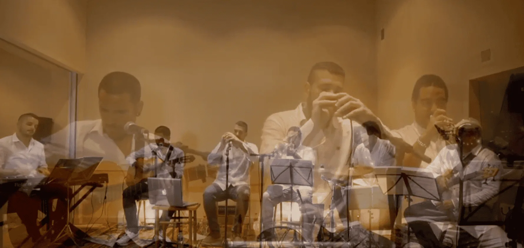 Cinco músicos en una sala interior, vestidos con camisas claras, tocando con micrófonos y atriles: a la izquierda un teclista, en el centro un guitarrista y un cantante de pie, y a la derecha dos músicos de viento. La imagen tiene un efecto de doble exposición que superpone primeros planos. Escena asociada a un trío de pop español y rumba para fiestas mayores en Barcelona.
